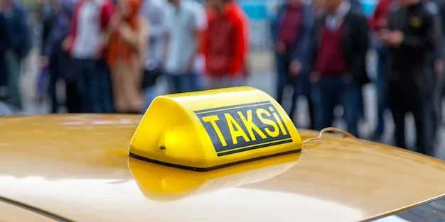 Kalabalık bir caddede sarı ticari taksinin tavanındaki TAKSİ tabelası